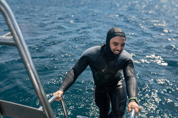 Smiling diver climbing boat ladder after scuba diving in ocean