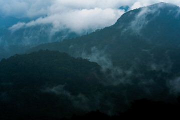 Mountains pierce the sky, wrapped in drifting clouds. Mist dances across ridges, veiling peaks in...
