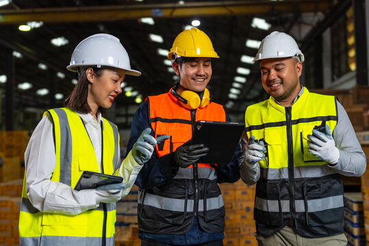 Professional asian engineer and technician wearing safety helmet analyzing meeting with tablet in factory warehouse. Confident factory workers group inspection industry factory. Teamwork concept.