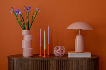 Detail of a sideboard styled with pastel candles, fresh flowers, and a modern lamp. Soft shapes and warm hues in a retro mood.