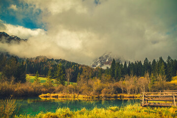A tranquil scene from Kranjska Gora, Slovenia, featuring a crystal-clear turquoise lake in the foreground.