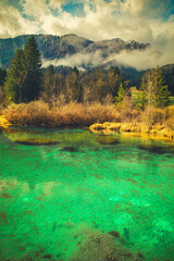 A tranquil scene from Kranjska Gora, Slovenia, featuring a crystal-clear turquoise lake in the foreground.