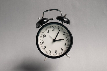 Black alarm clock in air on light grey background