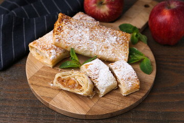 Tasty apple strudels with powdered sugar, mint and fruits on wooden table, closeup