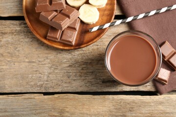 Tasty chocolate milk in glass, pieces and banana on wooden table, flat lay. Space for text