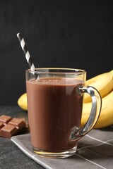 Tasty chocolate milk in glass cup, pieces and bananas on black table, closeup
