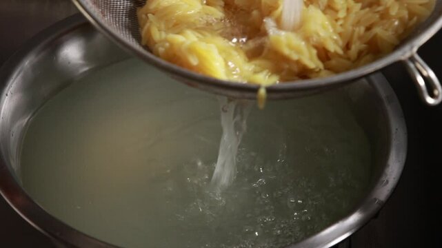 Close-up video of rinsing freshly cooked orzo pasta under running water in a strainer