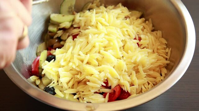 Close-up video of mixing a delicious orzo salad with fresh ingredients