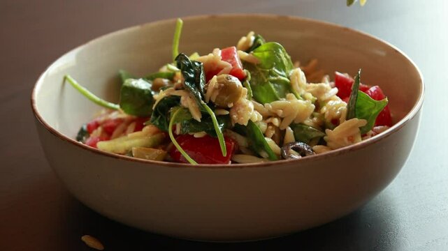 Close-up video of mixing a delicious orzo salad with fresh ingredients