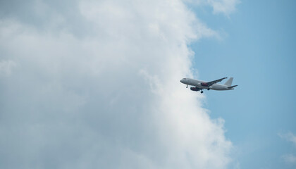 Passenger airplane, with landing gear down, approaches against a backdrop of blue sky and fluffy white clouds