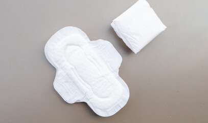 A series of sanitary pads stacked on a soft, neutral-colored surface, illustrating the essential nature of the product.


