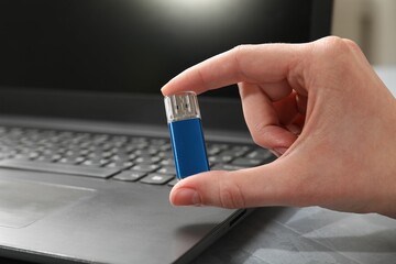 Woman with flash drive and laptop at gray textured table, closeup