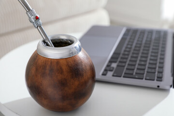 Traditional yerba mate tea and laptop on white table, closeup