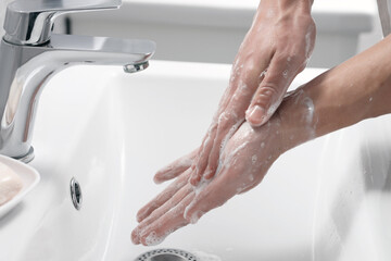 Woman washing her hands with foaming soap above sink in bathroom, closeup