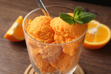 Balls of tasty orange sorbet in dessert bowl, fresh fruit and mint on wooden table, closeup