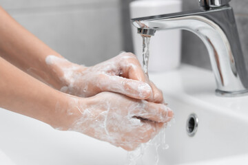 Woman washing hands at sink in bathroom, closeup