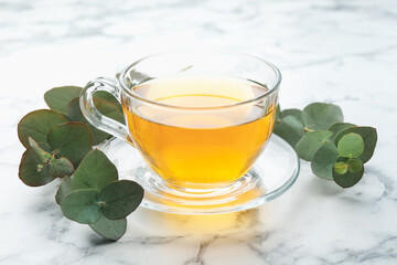 Aromatic tea in cup and eucalyptus branches on white marble table, closeup