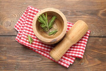 Mortar with rosemary, pestle and cloth on wooden table, flat lay