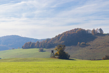 Hunting tower standing in a green field with autumn foliage in the background