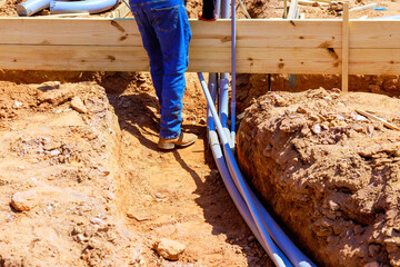 Construction worker positions wooden beams above foundation trench while laying out electrical pvc...