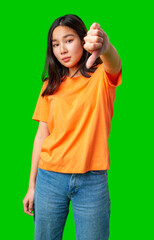 Young woman gives thumbs down gesture in bright orange shirt against green background