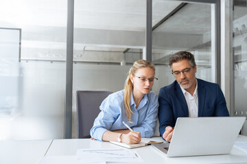 Mature focused senior mentor leader man showing young woman manager project on laptop in modern...