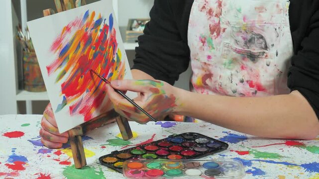 The hands of the artist, work to create creative images in art. Art paints and brushes, applying multi-coloured strokes to the canvas using palette, gouache and watercolour.