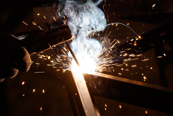 A man is welding a piece of metal with a bright orange flame