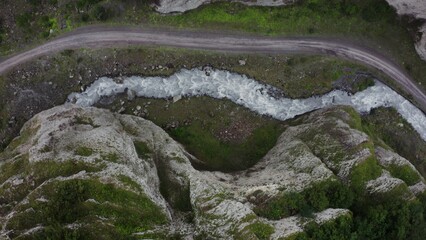 Top view of the seething mountain river and the road, in the lowland between the sheer cliffs, with a car standing on it
