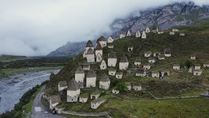 An ancient city of white brick towers on the hills near a seething mountain river, at the foot of rocky mountains, covered with thick clouds.
