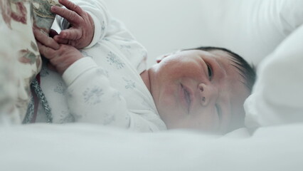 Newborn baby crying in bed, raising hands while expressing discomfort. baby's face shows distress,...