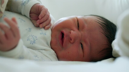 Newborn baby grimacing with eyes open, showing early expressions and movements during the first...