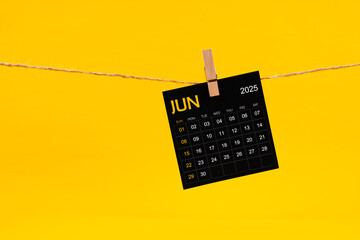 June 2025 black calendar hanged with brown rope on yellow.