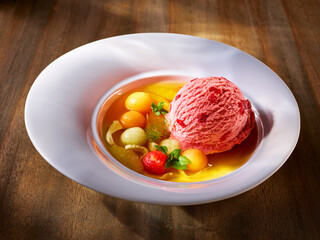 Erdbeereis mit Fruchtsuppe auf weissem Teller mit asymmetrischer Fahne, Dessertteller, Erdbeereis, Melonenkugeln, Obst