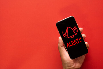 Hand holding mobile phone displaying alert notification, red bell icon with 