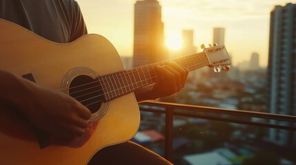 Close-up of a person playing an acoustic guitar outdoors on a city rooftop at sunset.
