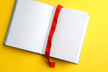 Open planner with red ribbon bookmark on yellow background, top view. Space for text