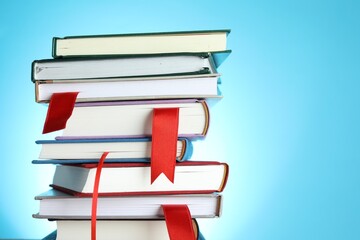 Books with red ribbon bookmarks on light blue background, closeup. Space for text