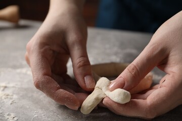 Woman making pretzel at light grey table, closeup