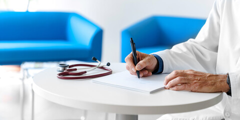 Doctor in a white coat with a stethoscope in a hospital writing a prescription. Doctor's hands...