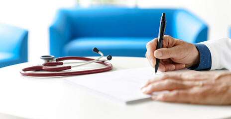 Doctor in a white coat with a stethoscope in a hospital writing a prescription. Doctor's hands...