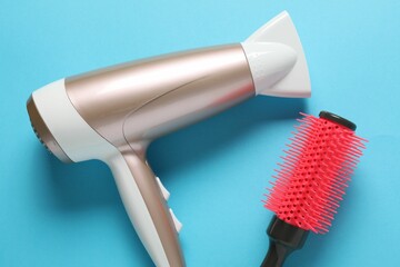 Hair dryer and brush on light blue background, top view