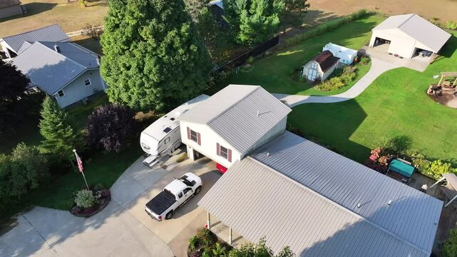 Aerial 360 degree view above a two floor rural home with a truck and camper parked outside and a fire pit, playground, shed, pole barn, and garden in the backyard.