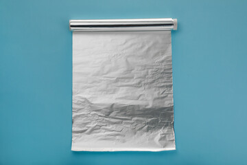 Roll of aluminum foil on light blue background, top view