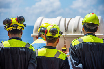 A group of sailors standing by the lifeboats, listening attentively to the deck officer&rsquo;s instructions on how to use the lifeboats and evacuate the ship, emphasizing safety training and preparedness.