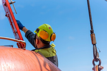 Crew member partially visible through the forward hatch of a lifeboat, closing the cover during an...