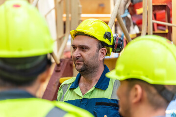 Marine engineer, merchant ship officer in blue overalls and yellow helmet explains lifeboat...