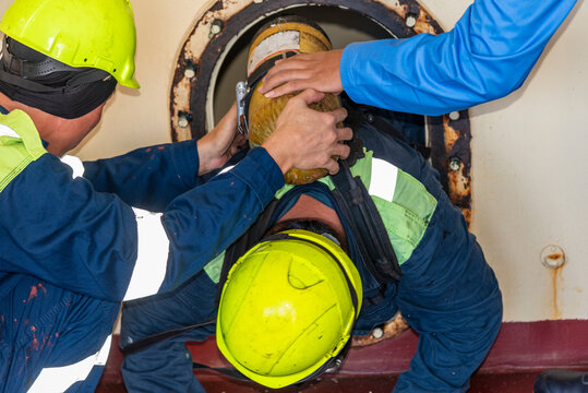 Crew member wearing breathing apparatus exits a narrow hatch after providing first aid during a man evacuation drill from a confined space on a merchant ship.