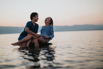 A cheerful couple enjoying moments together amidst tranquil waters and a beautiful sunset. The serene landscape sets a perfect backdrop for their joyful interactions and heartfelt shared moments.