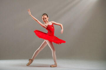 Young Japanese ballerina in red tutu and pointe shoes dances classical dance on light background.